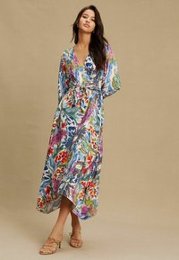 Ziedu raksta ietinamā kleita spilgtās krāsās, ar V-veida izgriezumu, garām piedurknēm, jostu viduklī un augstu-zemu apakšu. Gluda, viegla auduma.