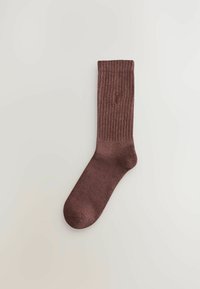 Burgunderfarbene gerippte Socke mit weichem Griff, verstärkter Ferse und Zehen, sowie einem dezenten Logo, das nahe der oberen Kante gestickt ist.