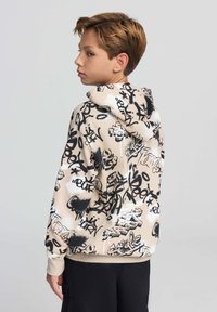 Felpa beige con motivi graffiti in bianco e nero, cappuccio con cordoncino, polsini e orlo a coste. Il materiale sembra morbido e informale.