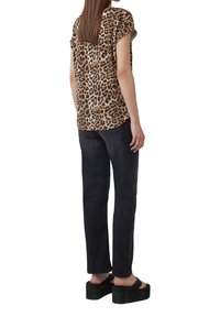 Blouse à manches courtes en imprimé léopard en tissu léger, associée à un jean noir à jambe droite et des sandales compensées noires.