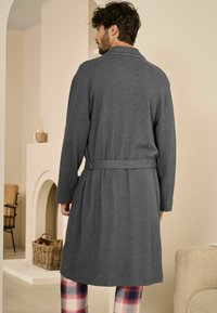 Herregrå morgenkåbe i mørkegrå farve, lavet af et tekstureret stof, med lange ærmer, knyttet talje og en afslappet pasform, kombineret med ternede pyjamabukser.