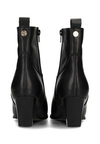 Bottines en cuir noir avec un talon épais, présentant une fermeture éclair et des accents de logo décoratifs à l'arrière. Texture lisse, design élégant.