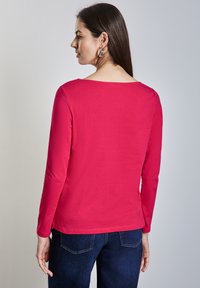 Długi rękaw, koszulka z okrągłym dekoltem w jasnoróżowym odcieniu, wykonana z bawełnianej mieszanki; gładka faktura z prostym krojem, w połączeniu z ciemnoniebieskimi dżinsami.