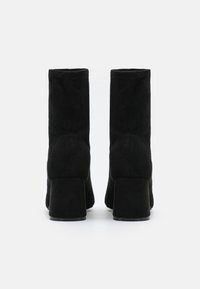 Bottines en daim noir à talon bloc, avec une texture lisse, un design minimaliste, sans éléments métalliques visibles ni ornements.