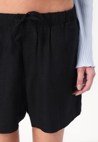 Czarne lniane szorty z elastycznym pasem i regulowanym sznurkiem. Charakteryzują się luźnym krojem i bocznymi kieszeniami. Gładka tekstura.