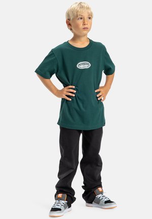Groene katoen t-shirt met een ronde hals en een wit logo, gecombineerd met zwarte broeken en grijze sneakers met oranje accenten en witte veters.