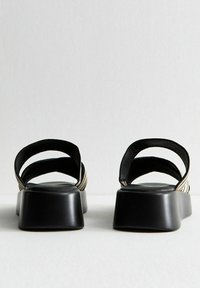 Zwarte platform sandalen met een kruisbandontwerp, matte afwerking en textuur bovenwerk. Beschikt over een brede, vlakke hak voor stabiliteit.