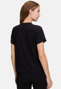 Svart t-shirt med kort ärm i bomull, med avslappnad passform. Har subtila dekorationer vid ärmsluten och en klassisk rundad halsringning.