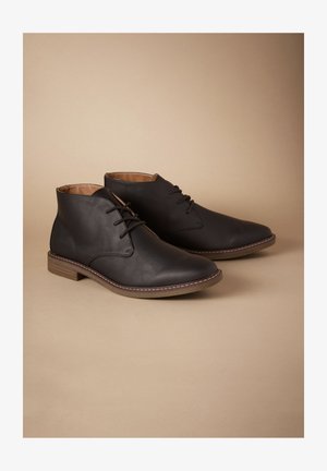 Schwarze Leder-Stiefeletten mit spitzen Zehen, Schnürdesign und hellbraunen Sohlen. Mit dezenten Nahtdetails entlang der Kante.