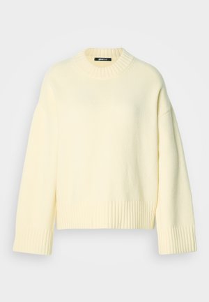 Kremfarget strikkegenser med ribbet rund hals og ribbede mansjetter, med løs passform og myk tekstur.