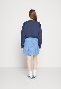 Laikakausi laivaston värisen lyhyt hiha sweatshirt, yhdistettynä siniseen kukkakuosiseksi hameeseen. Mallilla on valkoiset sukat ja hopeiset lenkkarit. Silkkiset kankaat.