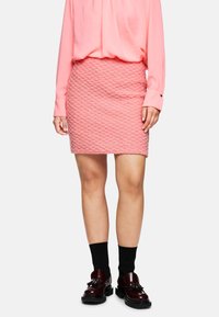 Rosa strukturierter Minirock mit einem Zickzackmuster, kombiniert mit einer rosa Bluse mit langen Ärmeln und dunklen Schuhen mit dicken Sohlen sowie schwarzen Socken.