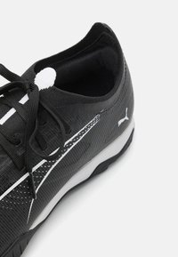 Sort athletic sko med struktureret overdel, hvide detaljer og snørebånd. Har en polstret inderside og en grå sål med rutedesign for godt greb.
