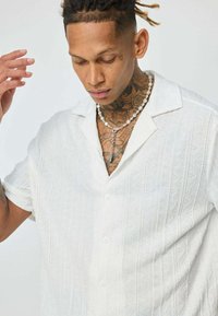 Chemise à manches courtes blanche avec un motif texturé et côtelé en tissu doux. Se caractérise par un col camp et un éclat subtil.