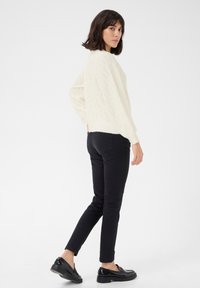 Cream cable-knit sweater with ribbed cuffs, paired with black slim-fit jeans and shiny black loafers. Simple design, neutral color palette.