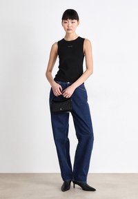 Zwarte mouwloze top met ronde hals, blauwe losse jeans, zwarte handtas en zwarte haklaarzen. Glad materiaal en casual ontwerp.