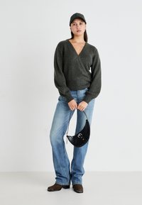 Temno zelena, volnena mešanica puloverja z V-izrezom in balonastimi rokavi, v kombinaciji s svetlo modrimi, nekoliko ohlapnimi jeans hlačami ter črno, teksturirano torbo.