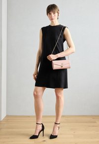 Schwarzes ärmelloses Kleid kombiniert mit einer pinkfarbenen, strukturierten Umhängetasche mit goldener Kettenriemen und einem Verschluss. Schwarze High-Heels.