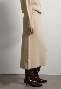 Suéter de punto beige y falda midi a juego. Puños y dobladillo acanalados y elásticos. Combinado con botas de charol burdeos hasta la rodilla, de puntera afilada.