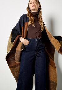 Multikleuren oversized poncho met bruine, zwarte en marineblauwe strepen, met een franjerand en van een warme, gestructureerde wolachtige stof.