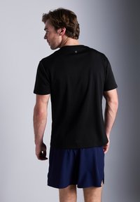 Zwarte T-shirt met korte mouwen, ronde hals, gemaakt van gladde stof. Draag het met marineblauwe shorts, met zijsplitten voor bewegingsgemak.