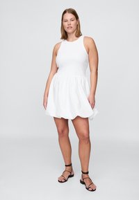 Biele šaty bez rukávov s priliehavým živôtikom a rozšírenou sukňou. Vyrobené z hladkej textílie, s okrúhlym výstrihom a jednoduchým dizajnom.