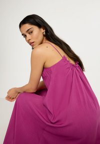 Vestido sin mangas de color rosa con la espalda fruncida, tejido fluido y tirantes ajustables. La textura suave realza la simplicidad del diseño en general.