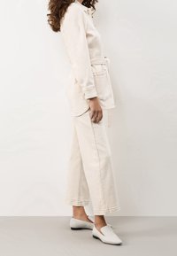 Beige denimjacka och korta byxor, båda i en avslappnad passform. Vita slip-on skor, slät textur, minimalistisk design.