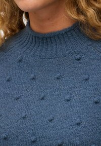 Niebieski sweter dziany z prążkowanym wysokim kołnierzem i teksturalnym wzorem w boble. Tkanina ma miękki, przytulny wygląd.