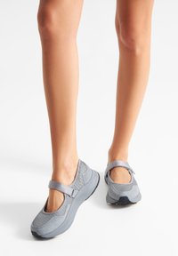 Zapatos estilo Mary Jane grises con parte superior de malla y suela sólida, que cuentan con una correa en el mediopie y un diseño de punta redondeada.