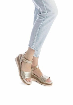 Sandalias beige con diseño perforado, correa al tobillo y suela de plataforma. Combinadas con jeans de mezclilla azul claro, mostrando la parte superior y los detalles.