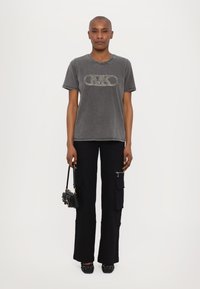 Camiseta gris de manga corta con detalle de logo brillante, combinada con pantalones cargo anchos negros con bolsillos y una cremallera plateada. Bolso y zapatos negros.