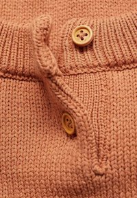 Knitted sweater in coral with a ribbed neckline. Features a round wooden button detail and a soft, textured finish.