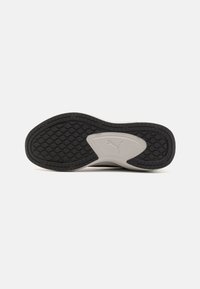 Suela de zapato de goma negra con un patrón texturizado, con un acento en la entresuela de color gris y un logo de Puma en relieve cerca del centro.