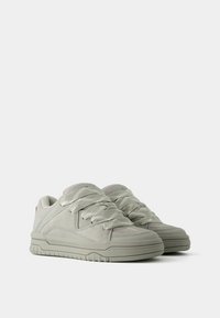 Szare sneakersy z teksturowaną powierzchnią i grubą gumową podeszwą. Posiadają szerokie sznurówki na wyściełanym języku oraz kanciaste akcenty w designie.