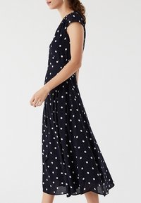 Granatowa sukienka w groszki, z krótkimi rękawami, dopasowaną talią i rozkloszowaną spódnicą sięgającą poniżej kolan.