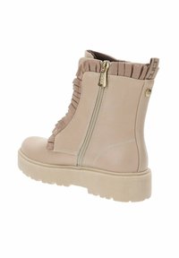 Botín beige hasta el tobillo con un acabado texturizado y brillante. Cuenta con un zipper lateral y un detalle de tela con volantes en la parte superior. Suela de goma gruesa.