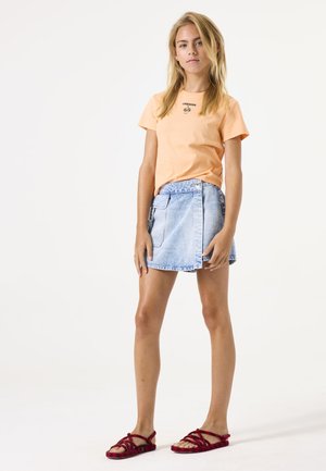 Lichtoranje katoenen T-shirt met de print "cherish"; blauwe denim wikkelrok; rode gevlochten sandalen met kruislings banden. Minimalistisch ontwerp, casual pasvorm.