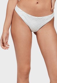 Bas de bikini blanc en tissu texturé avec des motifs en losange et de petits détails en œillet. Découpe offrant une couverture modérée sur les côtés.