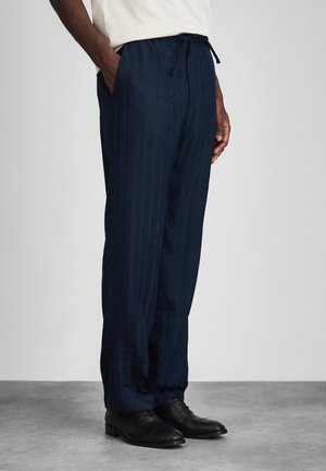 Navy patterned pants with a drawstring waist, subtle vertical stripes, side pockets, and a tapered fit, paired with black shoes.
