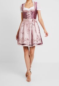 Robe dirndl en mauve et rose, avec des manches en dentelle, des broderies florales et un corsage ajusté avec des lacets. Jupe évasée avec un lien en ruban.