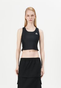 Melns īss tops no gludas auduma ar apaļu izgriezumu un nelielu trīsstūra formālo logotipu kreisajā pusē. Kopā ar melnu svārku.