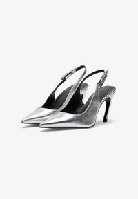Srebrne metalne slingback visoke pete z ostrimi nosi, elegantnim dizajnom in srednje visokimi stiletto petami. Prilagodljiv detajl okoli gležnja.