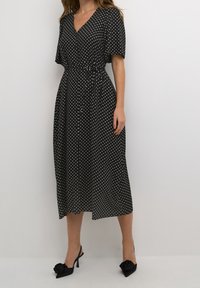 Mustapilkullinen midi-mekko, jossa on V-pääntie, lyhyet hihat ja solmittava vyötäröyksityiskohta, yhdistettynä mustiin avokkaisiin, joissa on kukkakoristeet.