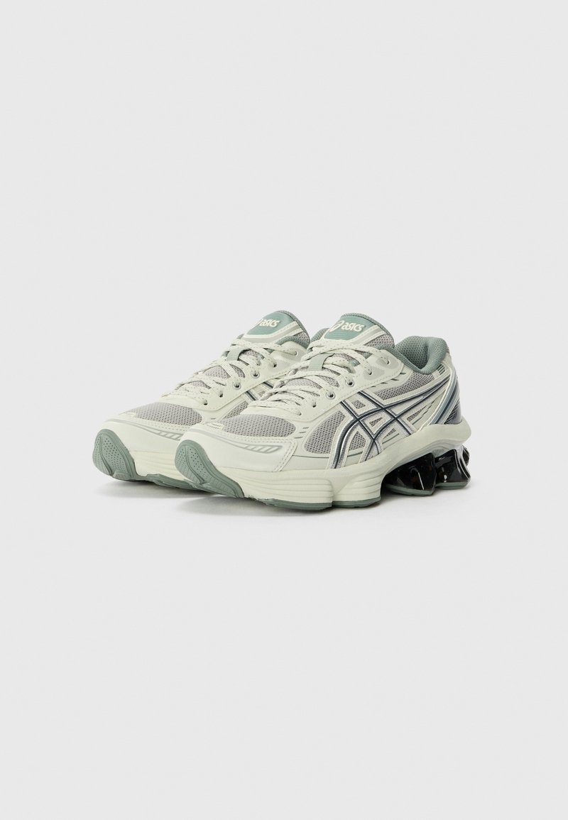 Baskets de sport gris clair avec un dessus en maille, accents verts et semelle en gel noir amortissante. Équipées d'un système de laçage et de marquages sur la languette.
