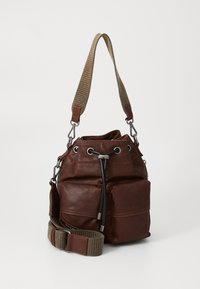 Brown leather bucket bag with front pockets, black drawstring closure, and wide beige fabric shoulder strap with leather accents.