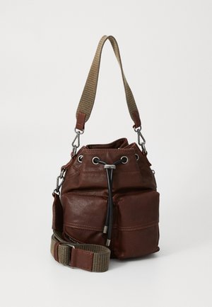 Brown leather bucket bag with front pockets, black drawstring closure, and wide beige fabric shoulder strap with leather accents.