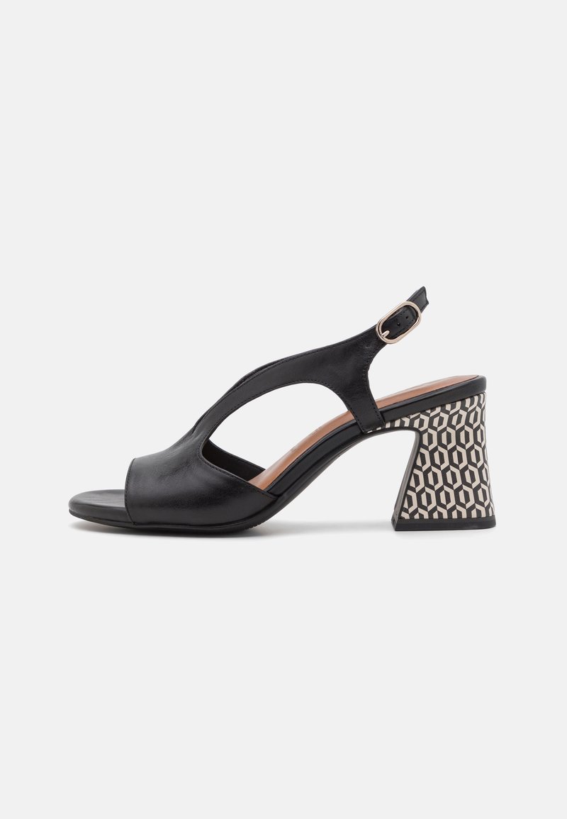 Svarte lær slingback-sko med åpen tå og en geometrisk mønstret blokkhelt i hvitt og svart. Justerbar ankelstropp for bedre passform.