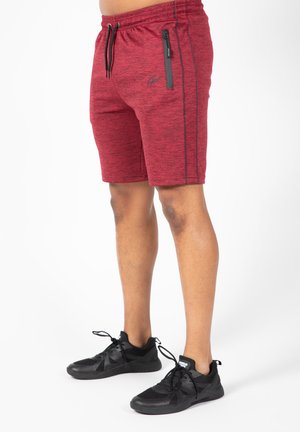Shorts de sport rouges avec un motif chiné, dotés d'une taille élastique et d'une poche zippée noire. Portés avec des baskets noires.
