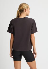 T-shirt oversize grigio scuro con maniche corte, scollo tondo e design semplice. Abbinato a pantaloni ciclisti neri a coste.